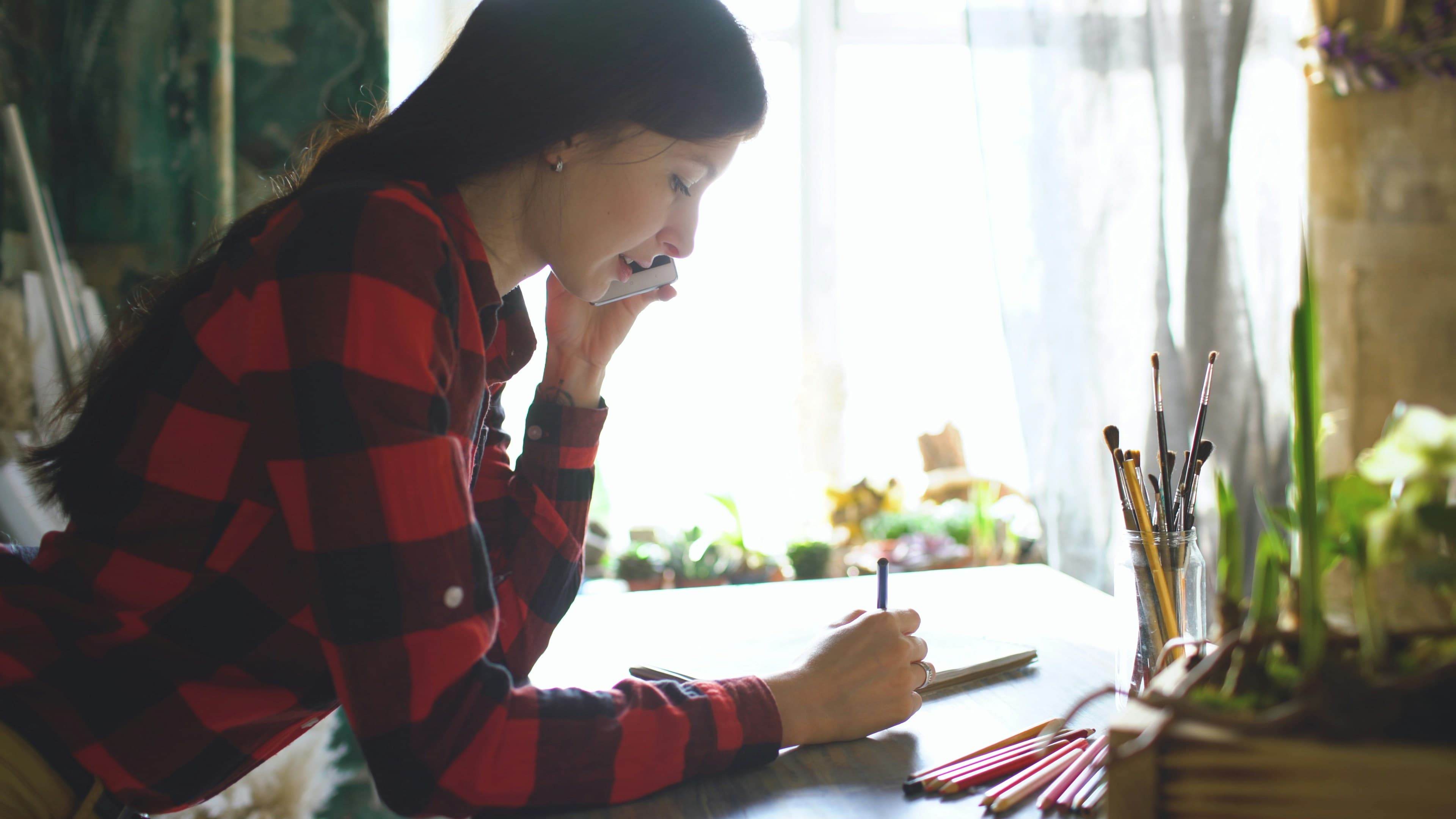 Young woman on phone, sketching in notebook