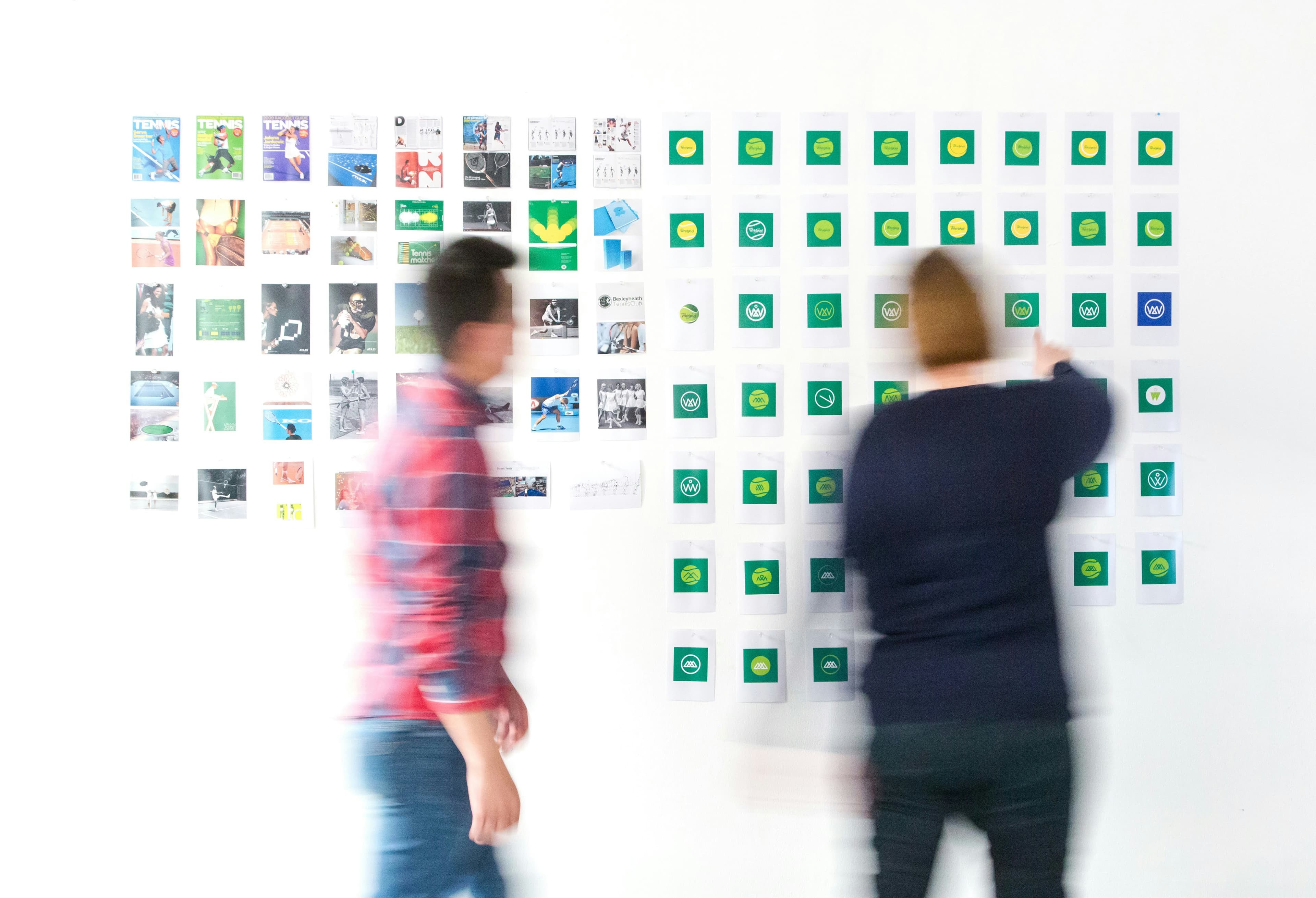 Two blurred people standing before a wall covered in small printed images and logos