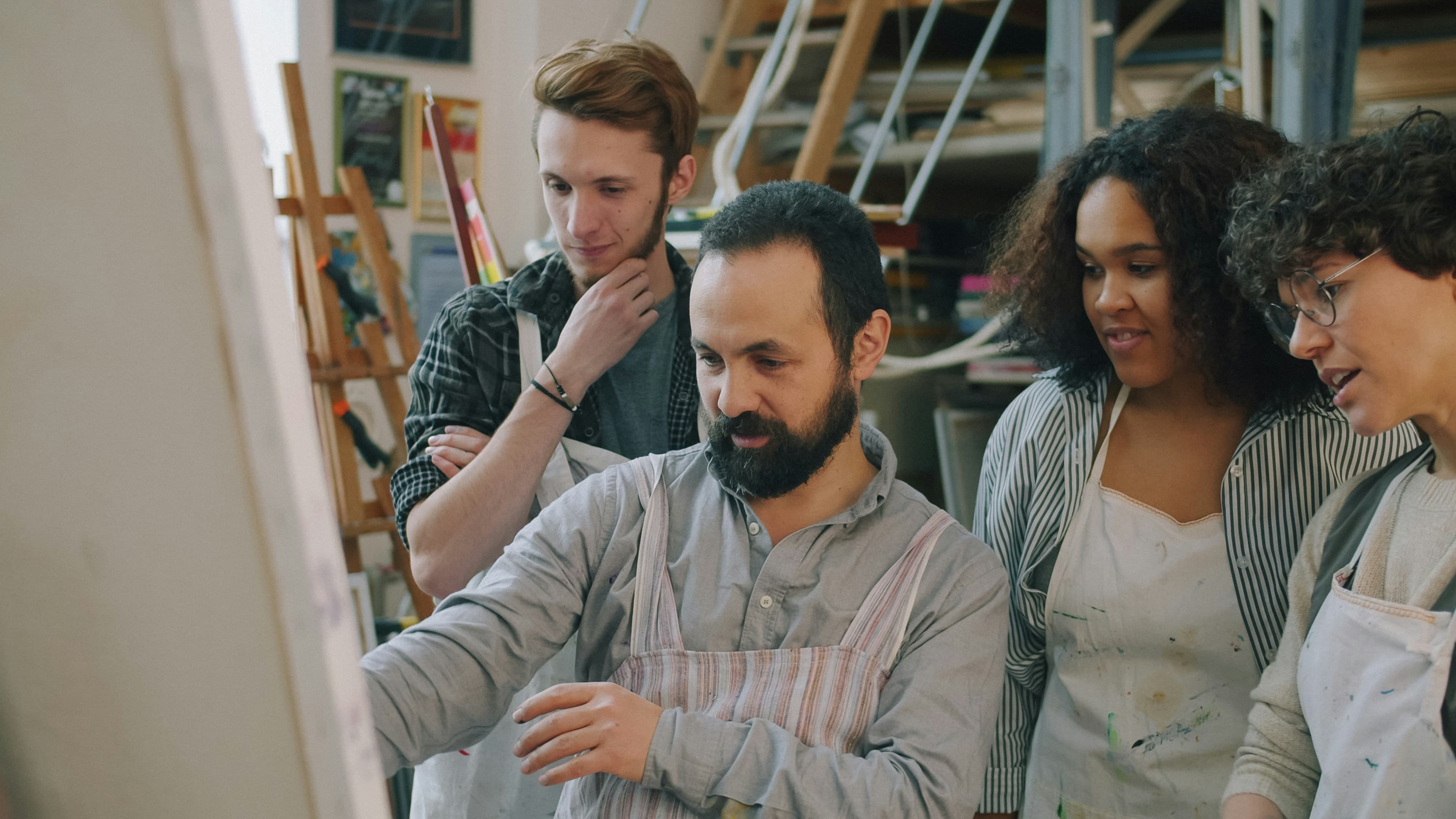 A group of four people in aprons looking at a canvas in an art studio