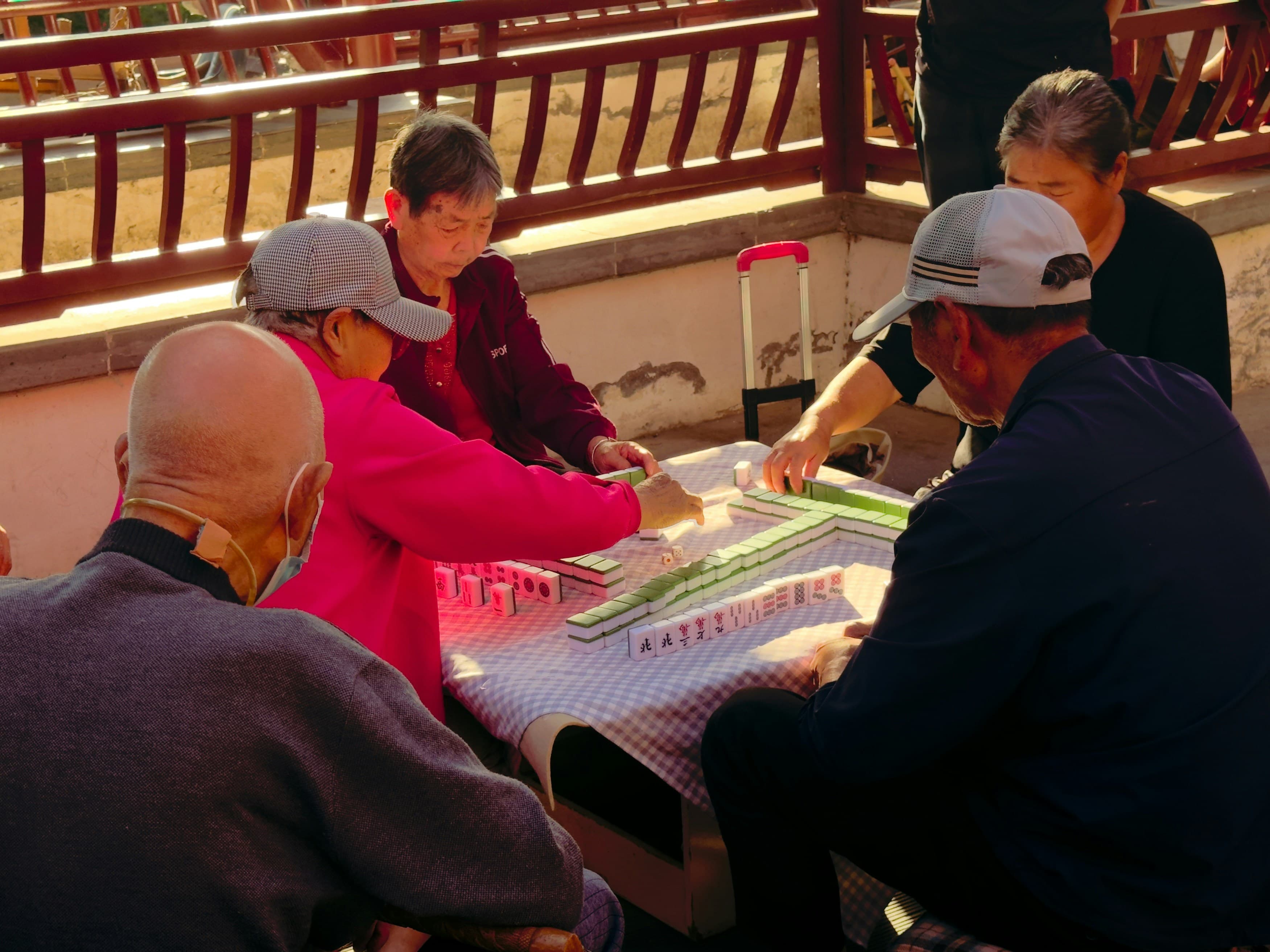 Elderly people playing mahjong on a table outdoors
