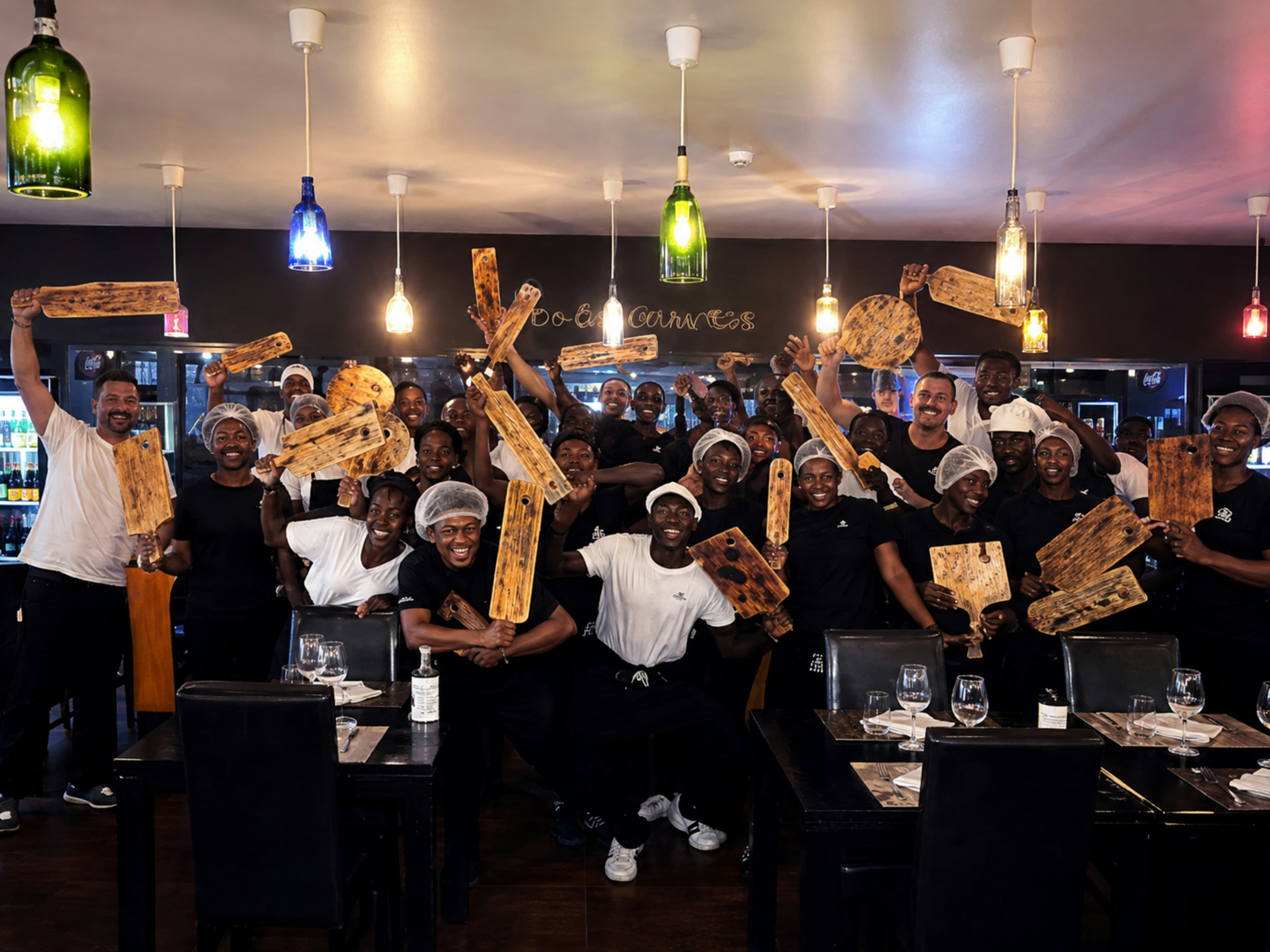 A large group of restaurant staff holding wooden serving boards in a dining room
